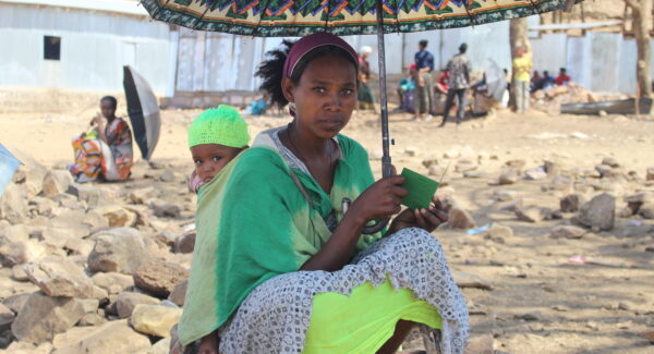 woman with child in the shade under an umbrella at refugee camp in Tigray