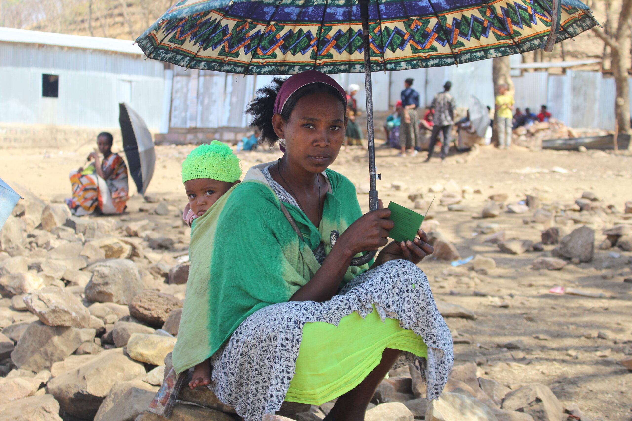 woman with child in the shade under an umbrella at refugee camp in Tigray