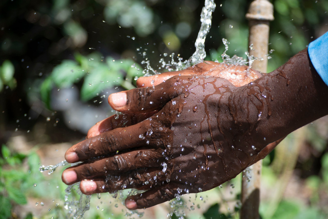 pair of hands cups water from a borehole