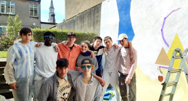 fine artist poses with Clongowes art students with the painted mural behind group