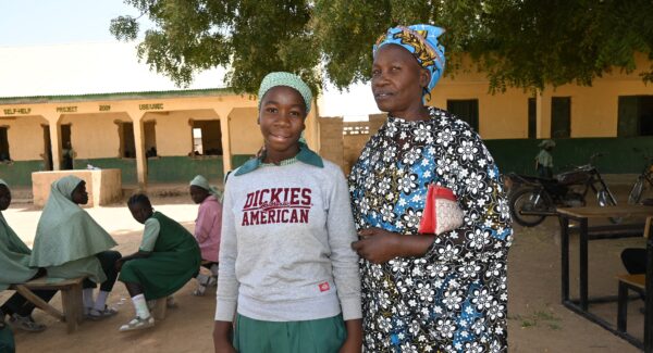 Sarah, a teacher poses for photo outside with student