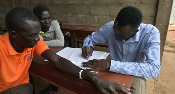 Teachers training. Two men sit at a school desk looking over a paper or textbook