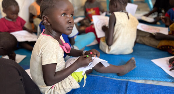 Sudan Crisis girl sits on floor of reception tent at Renk for refugee registration and processing