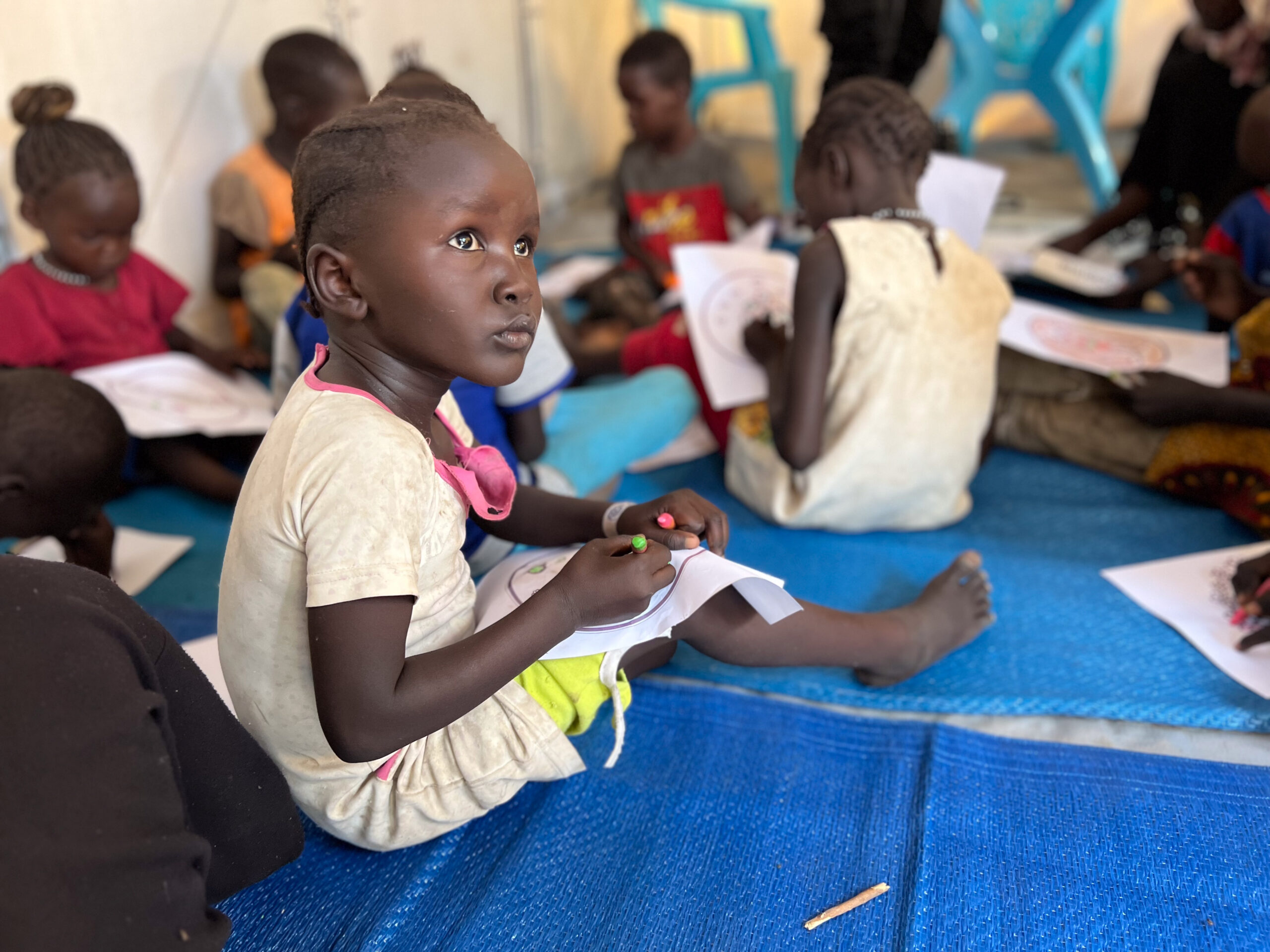 Sudan Crisis girl sits on floor of reception tent at Renk for refugee registration and processing