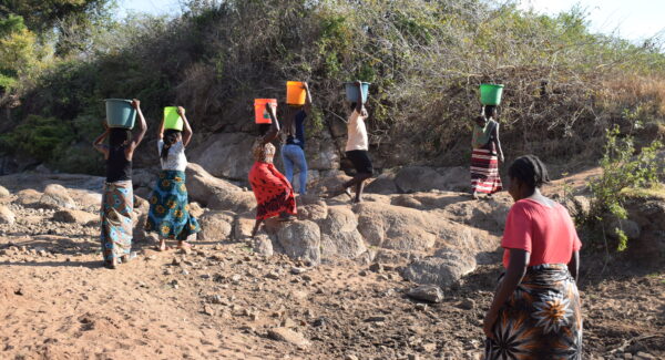 women collecting water from river in Thiba village, Malawi. they walk with buckets carried over their heads.
