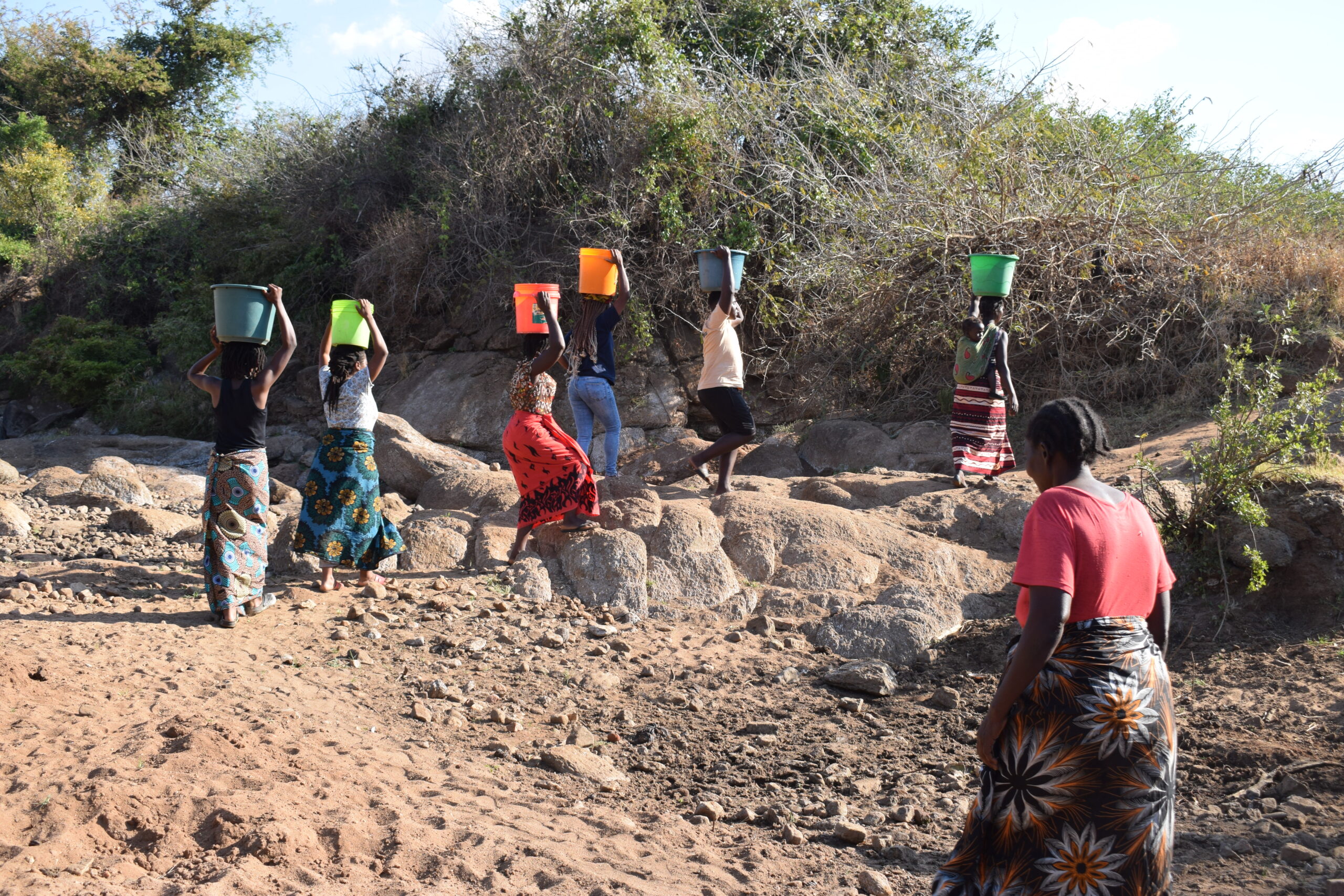 women collecting water from river in Thiba village, Malawi. they walk with buckets carried over their heads.