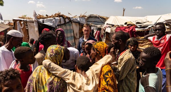 Shane Burke stands in refugee camp, an injured man is being carried into a medical tent.