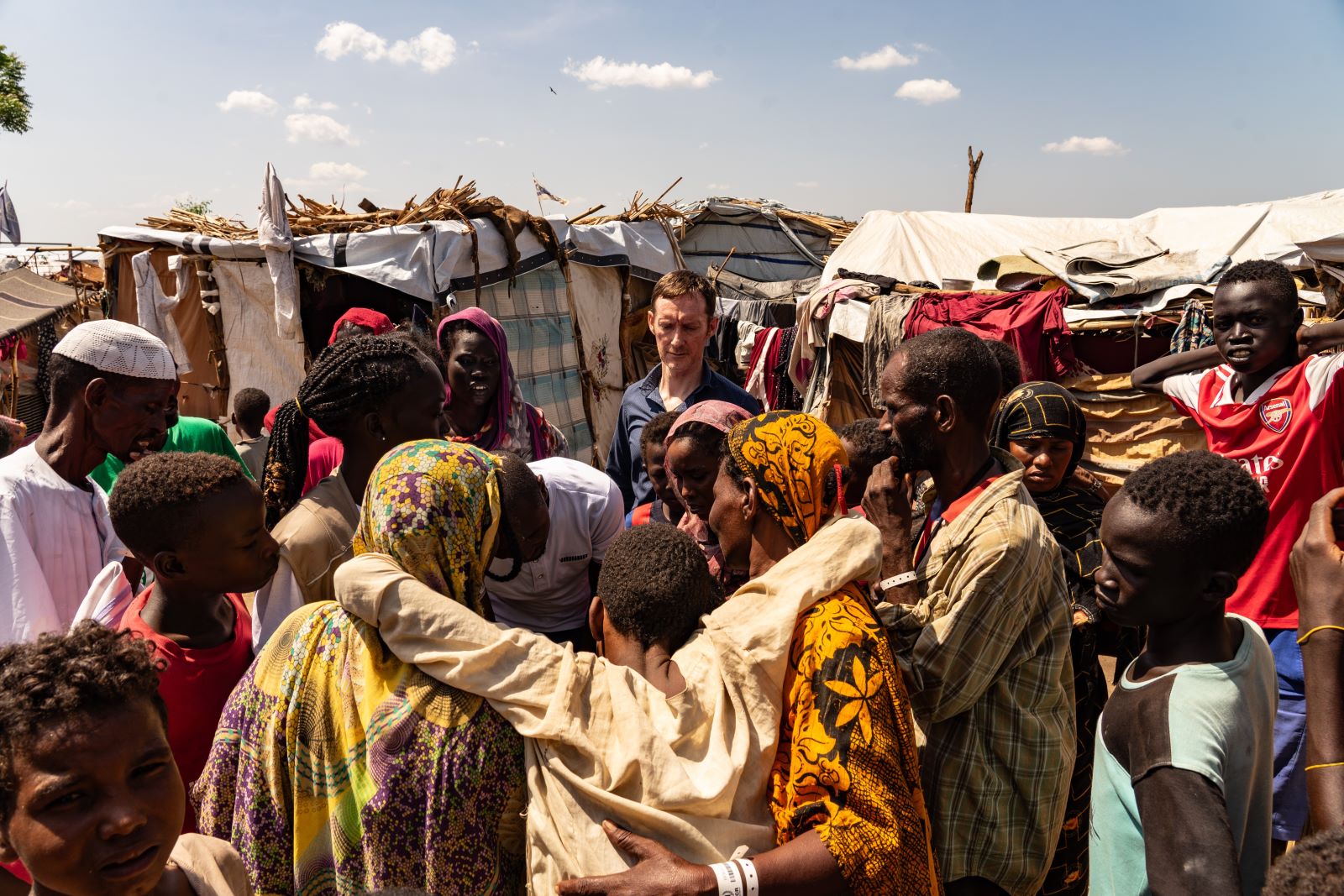 Shane Burke stands in refugee camp, an injured man is being carried into a medical tent.