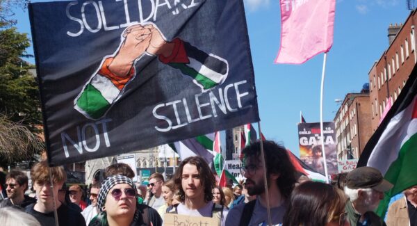 Palestine solidarity march in Dublin on 20th April 2024. A sigh reads 'solidarity not silence' around an image of two shaking hands. one sleeve is the Irish flag, the other sleeve is the Palestine flag.