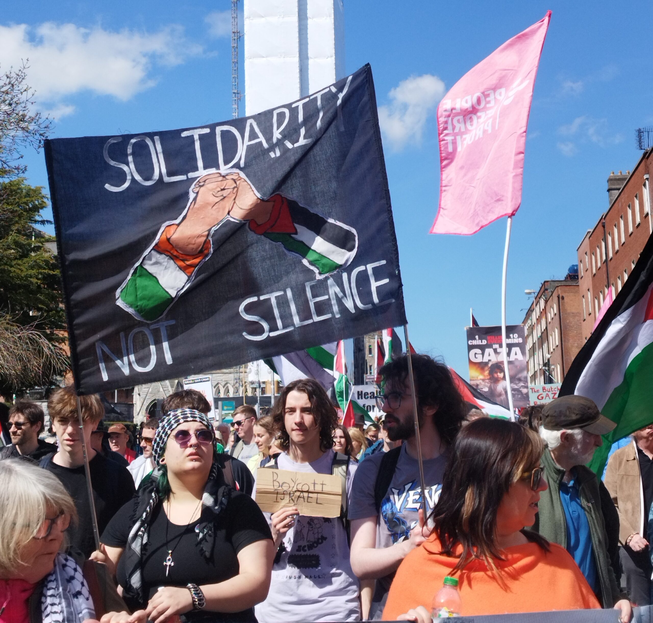 Palestine solidarity march in Dublin on 20th April 2024. A sigh reads 'solidarity not silence' around an image of two shaking hands. one sleeve is the Irish flag, the other sleeve is the Palestine flag.