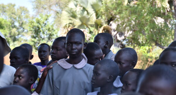 school girl gazes to camera. she stands outside in her uniform with her classmates.