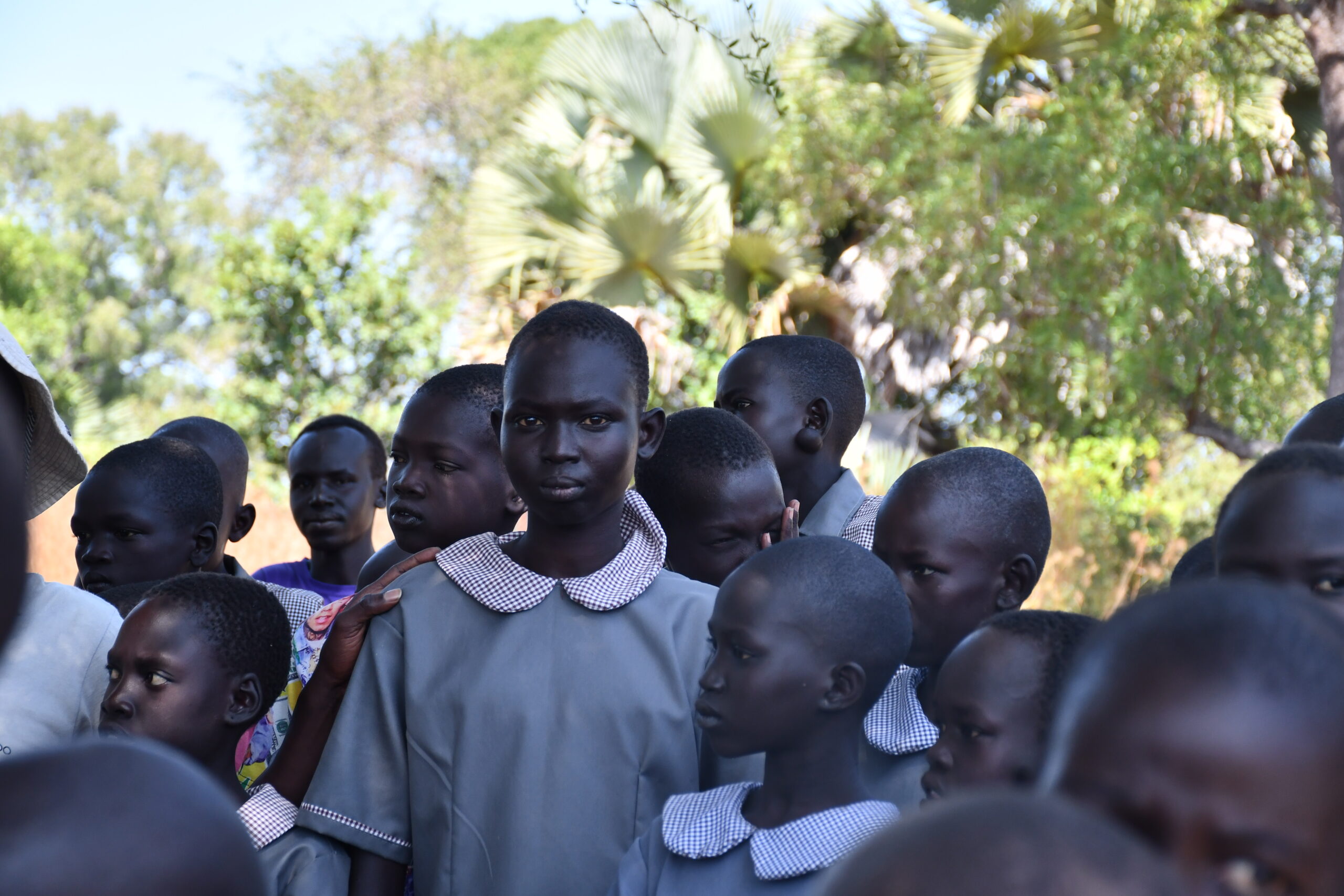 school girl gazes to camera. she stands outside in her uniform with her classmates.