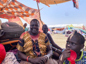 Duck, a refugee, smiles at camera outside her tent in Renk.