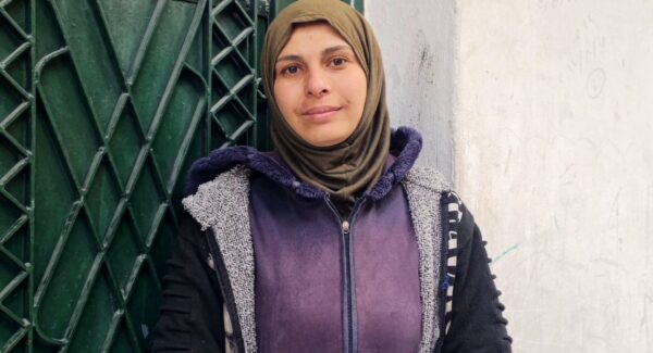Sarah, a mother in Aleppo, looks toward camera whilst standing in a doorway.