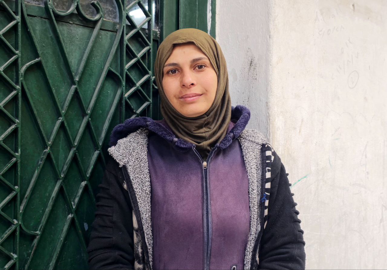 Sarah, a mother in Aleppo, looks toward camera whilst standing in a doorway.
