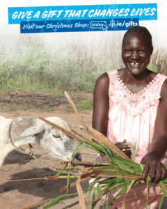 Martha, a woman farmer in South Sudan smiles at camera while feeding her goat