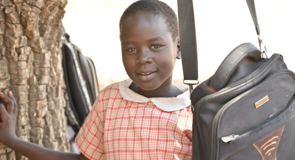 Elisabeth, a school girl, smiles at the camera under a tree in South Sudan.