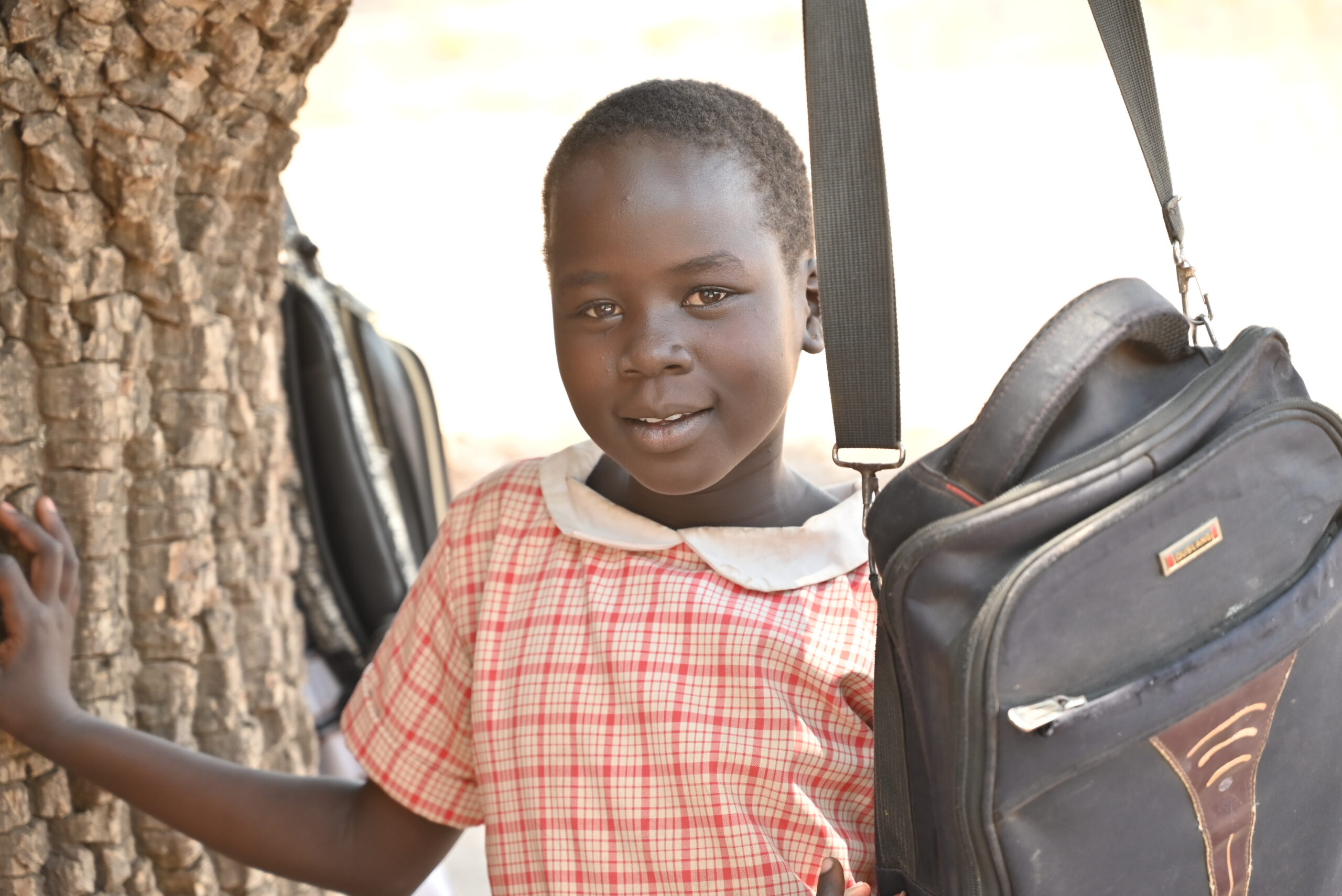 Elisabeth, a school girl, smiles at the camera under a tree in South Sudan.