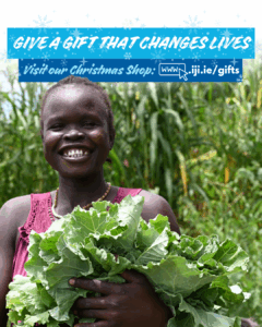 a womna farmer from South Sudan, smiles at the camera as she holds cabbage she has grown in her hands
