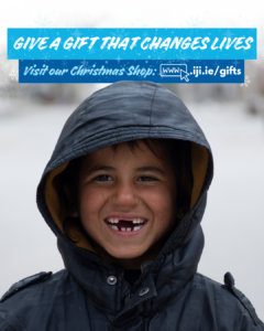 a Syrian boy smiles to camera in a winter coat. he has missing teeth