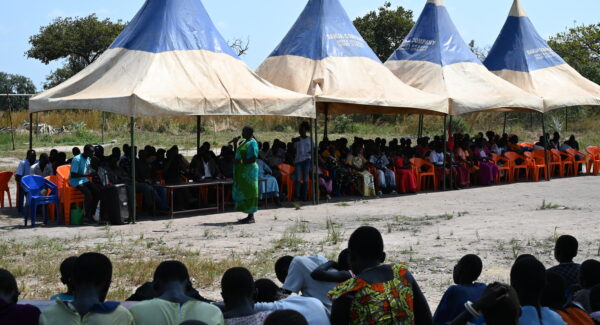Community of Akol Jal gather together for speeches. the majority of the village sit under a large pavilion tent.