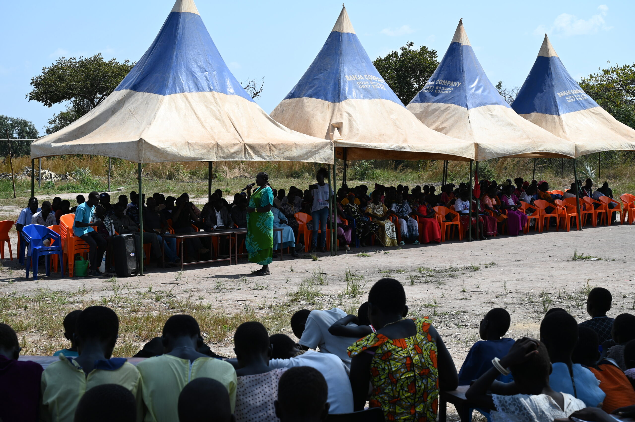 Community of Akol Jal gather together for speeches. the majority of the village sit under a large pavilion tent.