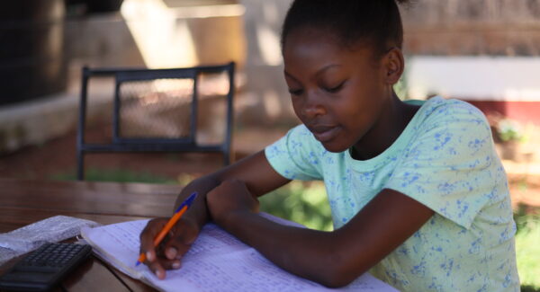 Faith, a girl child, sits at wooden desk, she is doing her schoolwork