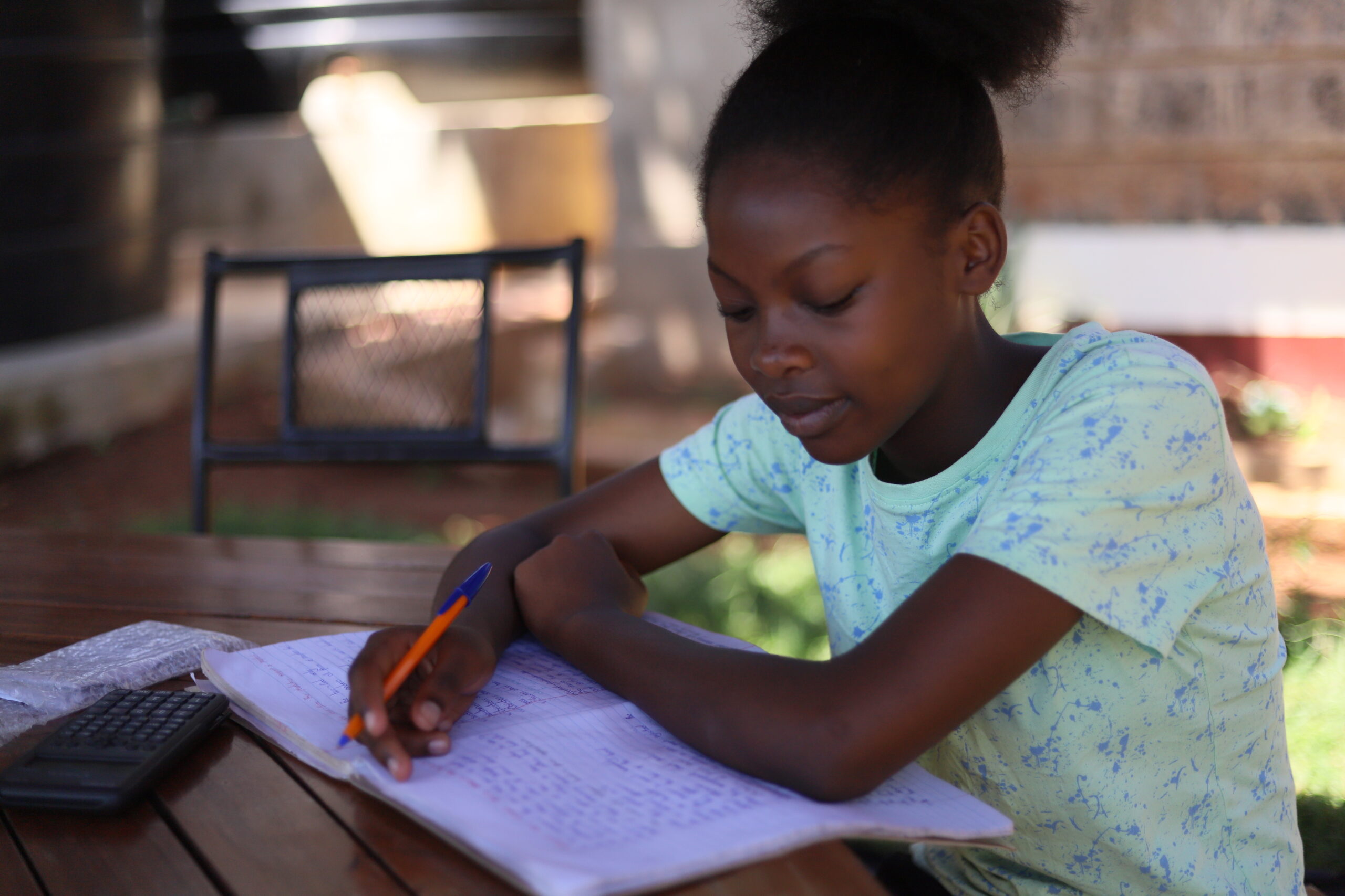 Faith, a girl child, sits at wooden desk, she is doing her schoolwork