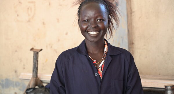 Martha, a trainee mechanic in South Sudan, smiles at the camera. she is wearing navy overalls