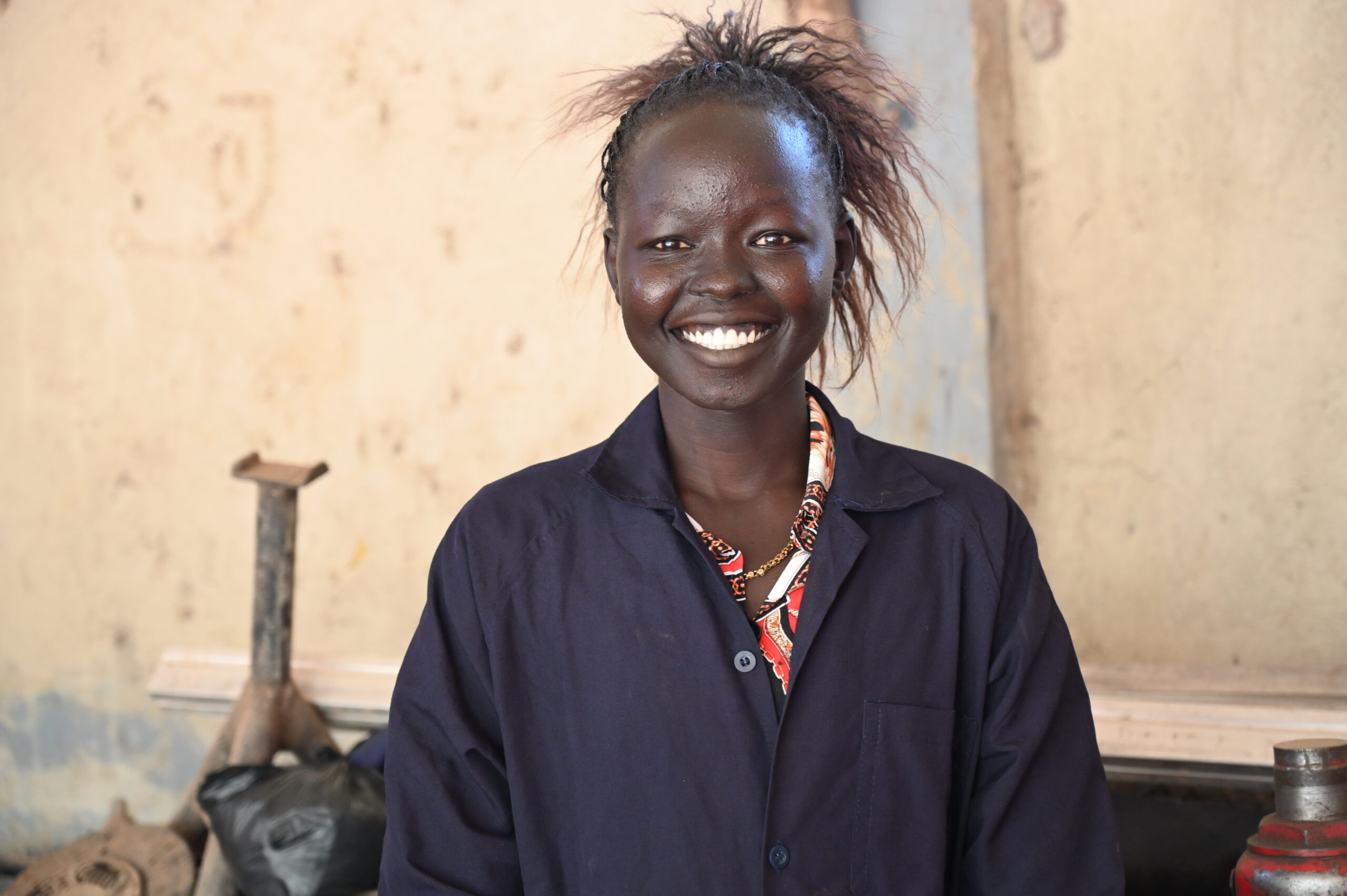 Martha, a trainee mechanic in South Sudan, smiles at the camera. she is wearing navy overalls