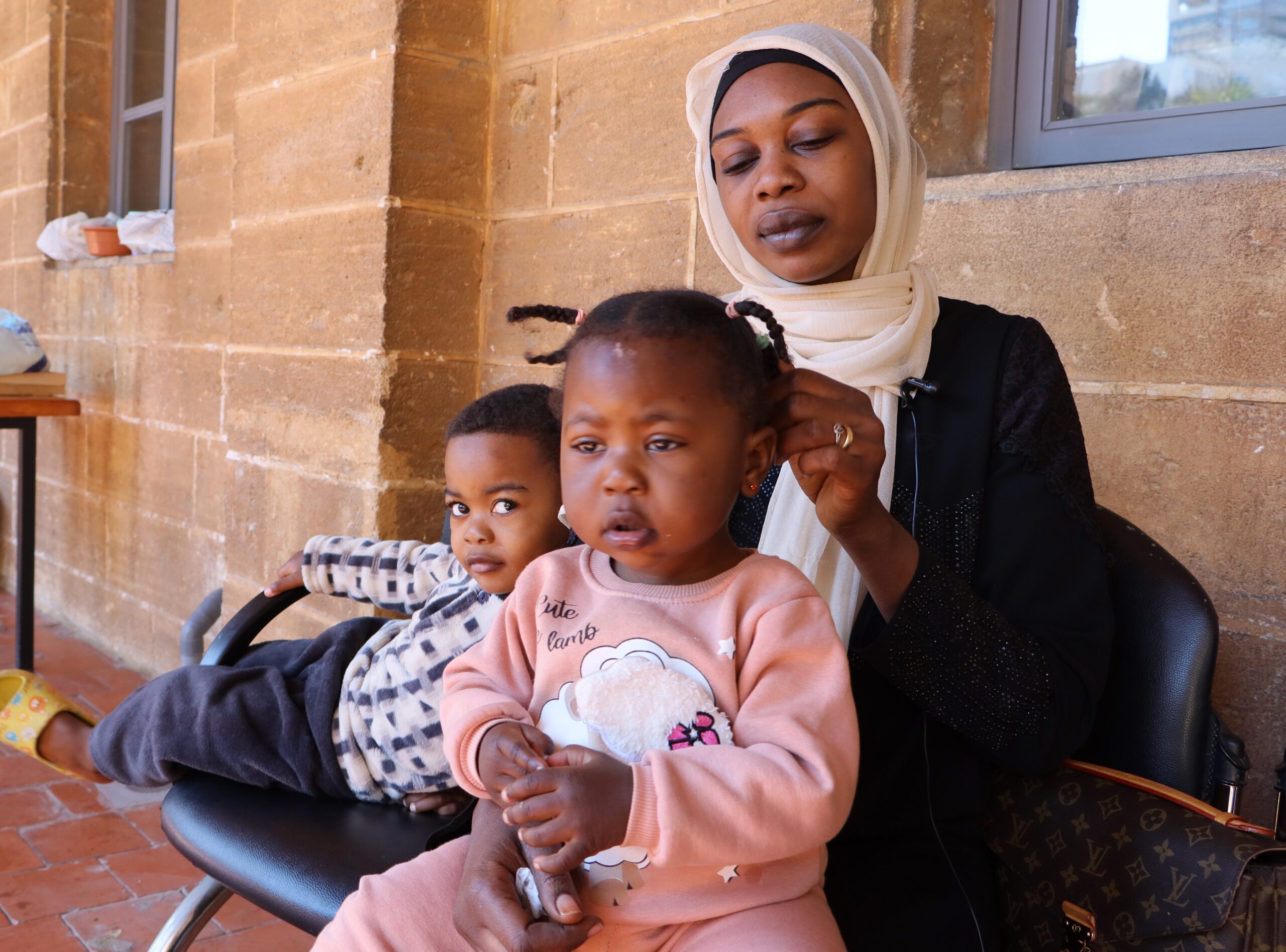 Zahraa is sat on a chair with her children. her daughter sits on her lap.