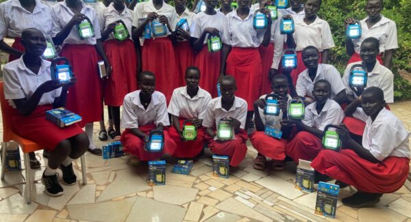 a group of students in uniform smile at the camera. they are holding their solar lamps